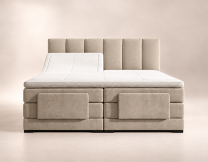 
Beige Lumière elektrische boxspring met hoofdbord met verticale banen, witte topper en verhoogde linkerbedhelft in een lichte studio.